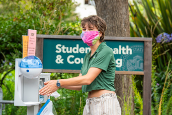 Student with a mask cleaning hands at a sanitation station