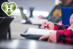 Photo of a students notebook and hand writing with plaid heart in the upper left hand corner