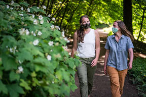 two people with masks on walking on a trail